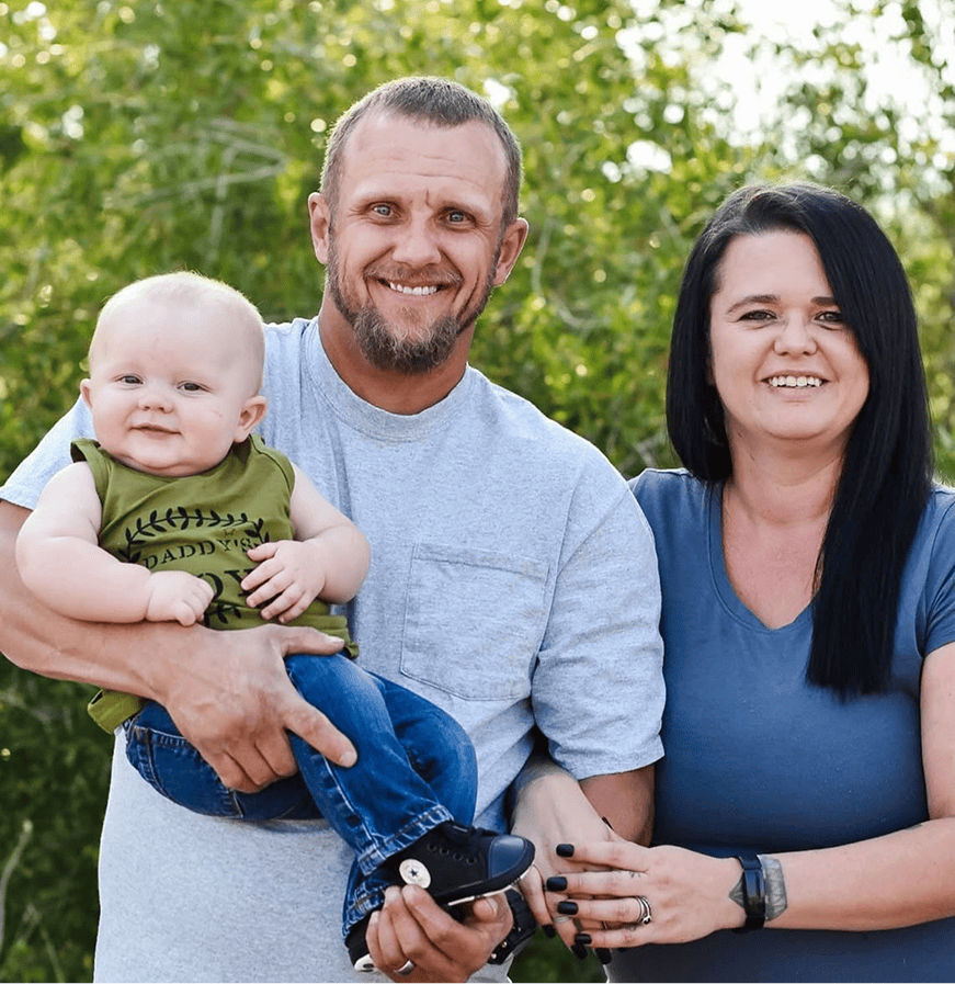 Family outdoor portrait with parents and baby in a park. Smiling family enjoying a sunny day surroun.