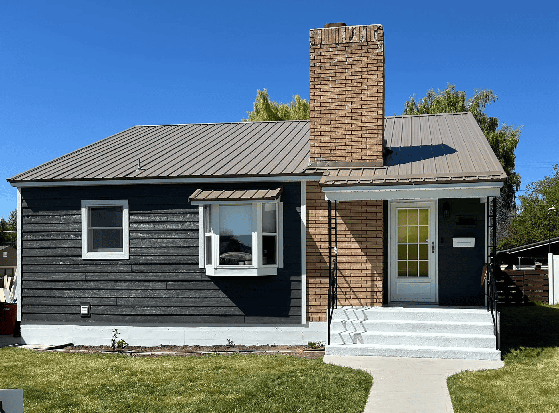 Modern house with brick chimney and gray siding, front yard, and clear blue sky.